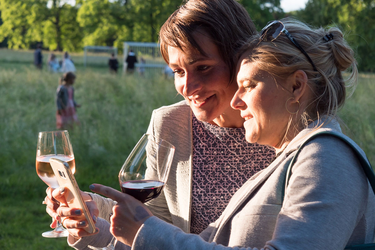 zwei Frauen mit Weingläsern schauen auf ein Smartphone